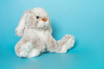 Stuffed bunny on blue background. Easter concept. Cute white toy bunny sitting on colored...