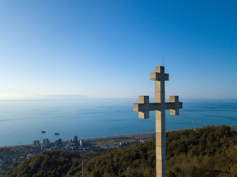 Close-up view from a drone of an Orthodox cross on a mountain against the background of the sea, a city on a sunny evening, Georgia. Concept of freedom, Christianity, Orthodoxy