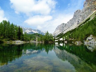 Beautiful double lake in Triglav lakes valley in Triglav national park and Julian alps in Gorenjska, Slovenia with larch trees and leftover snow and a reflection of the mountains in the lake