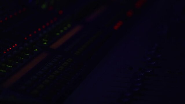 The red signal lights of the sound engineer's console flash in the dark, the sound console is illuminated by blue light from the stage.