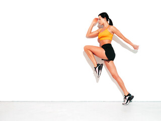 Fitness woman in sexy sports clothing. Young beautiful model with perfect body. Female posing in studio near white wall at summer sunny day. Jumping and running