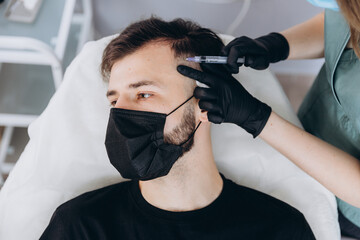 Mesotherapy procedure. A cosmetologist performs a mesotherapy procedure on the head of a young man....