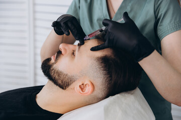 Mesotherapy procedure. A cosmetologist performs a mesotherapy procedure on the head of a young man....