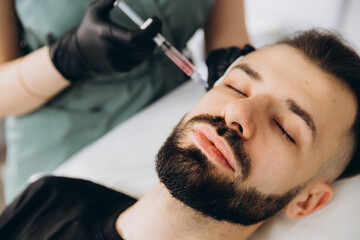 Obraz na płótnie Canvas An attractive man receives mesotherapy injections to treat hair loss at the clinic. Injections into the skin and scalp