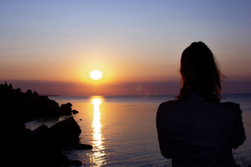 Silhouette of a girl on a background of dawn. The outlines of the rocks 