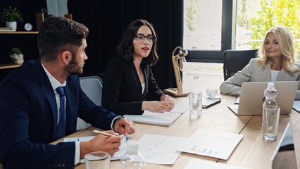 young businesswoman in eyeglasses talking to colleagues in meeting room