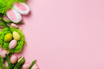 Easter composition. Colorful eggs in a nest of tulip flowers rabbit ears on a pink background copy space