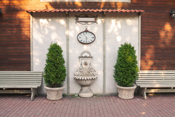 Fragment of landscape design of the park. Garden fountain, potted trees, wall clock.