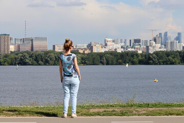 Girl standing on background of river and buildings of Moscow city. Real estate concept, travel and holidays at summer