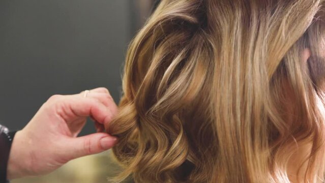 A curl on the head of a girl with brown hair is corrected by a hairdresser, sprays with varnish and combs with a comb on a gray background. High quality FullHD footage