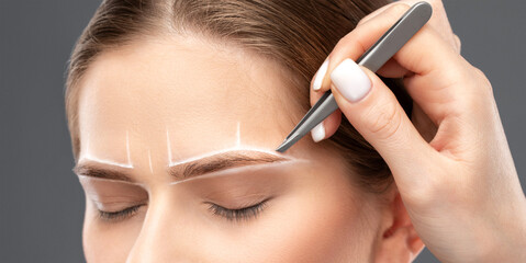 Makeup artist plucks eyebrows in a beauty salon. Professional makeup and cosmetology skin care.