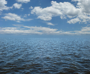 Obraz premium Simple rippling water and fluffy clouds nautical message background - blue sky and puffed clouds with ocean beneath ideal for a marine theme fishing, vacation, nature or weather message 