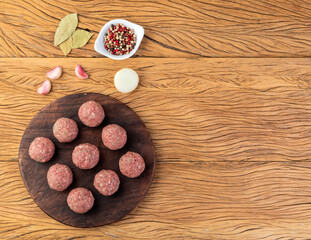 Raw meat balls over wooden board with seasonings and copy space