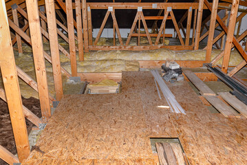 Unused attic with visible trusses, mineral wool and OSB boards lying on the ceiling beams.