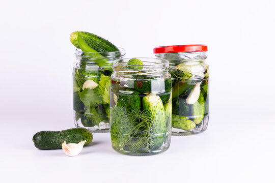 Pickled cucumbers in glass jar with fresh cucumbers, peppers and garlic on white background.