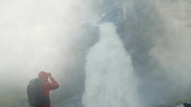 Photographer with backpack takes picture of epic waterfall