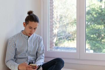 Young man sitting winged from the window using the smartphone