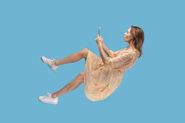 Hovering in air. Surprised shocked girl in dress levitating with mobile phone, chatting online in...