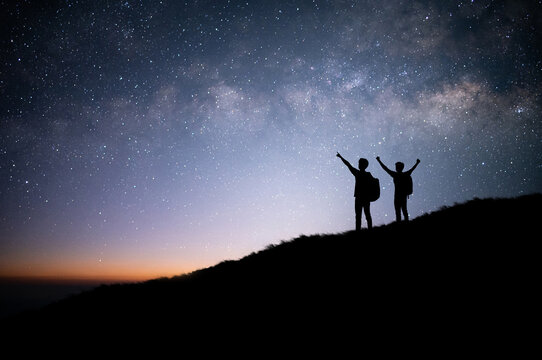 Silhouette of two tourists standing and watched the star, milky way and beautiful view night sky on top of the mountain. They are enjoyed traveling and was successful when he reached the summit.