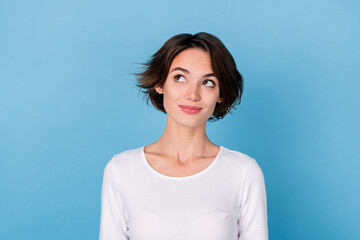 Photo of dreamy adorable young woman wear white shirt smiling looking empty space isolated blue...