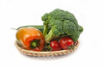 Fresh broccoli, cucumber, pepper and tomatoes on a wicker basket on white background