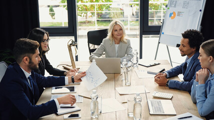 young businessman holding infographics during meeting with multiethnic colleagues