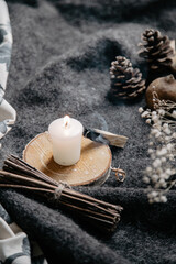burning candle on a winter table with whool, pine cone and tea cup