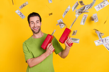 Photo of joyful beard millennial guy with money gun wear green t-shirt isolated on yellow color background - obrazy, fototapety, plakaty