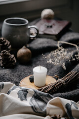 Fototapeta na wymiar burning candle on a winter table with whool, pine cone and tea cup