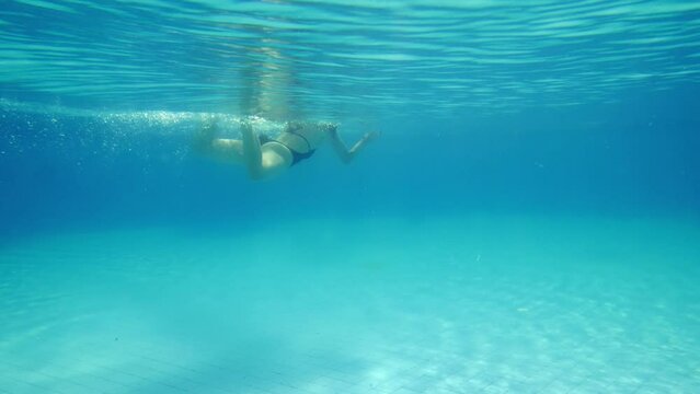 The woman stands poised on the edge of the pool, leaning forward and dives into the water, camera also plunges into the water and shows shortly the swimmer's movement underwater