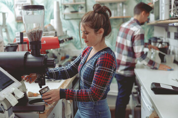 Fototapeta na wymiar Portrait of focused lady barista standing near coffee grinder in coffee shop