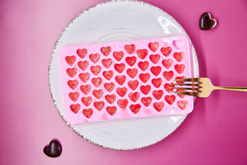 Creative pink frozen ice hearts on white plate with fork. Creative romantic dinner, Valentines Day concept. Pink gradient background. Top view.