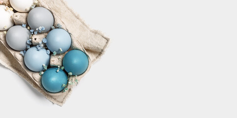 Close up Easter eggs pastel colored in egg box decorated small flowers. Minimal Easter celebration concept, dyed chicken egg with blue green color gradient in carton pack. Top view