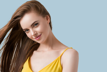 Beautiful brunette with long smooth hair in yellow dress natural portrait. Color background. Blue