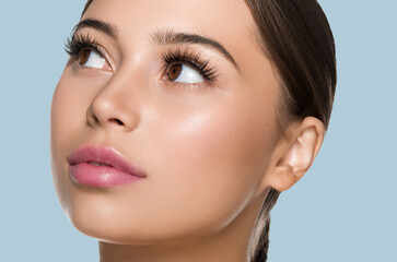 Woman skin face with lashes beautiful eyes healthy hair brunette. Look up. Color background. Blue