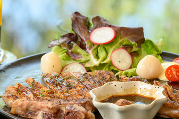 Roasted steak pork, grilled pork chops with vegetable salad and toast bread with steak sauce in black plate on the dining table food
