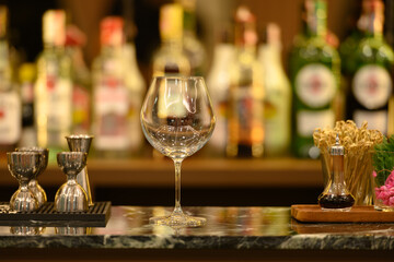 clear glass on black marble table top and beautiful bokeh shelves with alcohol bottles