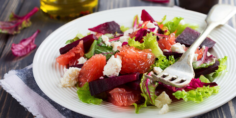 Salad of beets, lettuce, beetroot leaves, grapefruit and feta cheese on the old wooden background. Selective focus.
