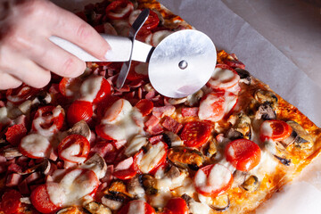 Hand with pizza cutter knife cutting pizza at kitchen table. Close up