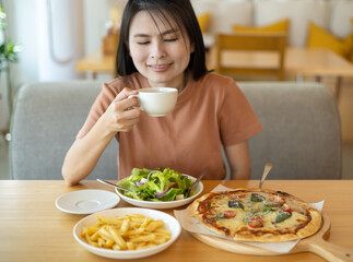 A woman drinking coffee with feeling happy and enjoy to eat food in the restaurant in leisure time. dine in the restaurant, eating delicious served hot pizza and salad. Eating concept. Italian food.