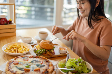 Close up of young woman eating hamburger and salad at restaurant with feeling happy and enjoy to eat. Italian food. Enjoy eating concept. Back view.