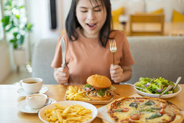Young Asian woman smiling with her food, pizza, hamburger, A woman holding fork and steak knife feeling happy and enjoy to eat food in the restaurant. Enjoy eating concept. Italian food.