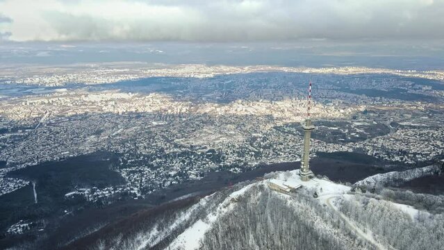 Aerial Winter view of Kopitoto tv tower, Vitosha Mountain, and city of Sofia, Bulgaria. Stunning drone footage. Cloudy sky