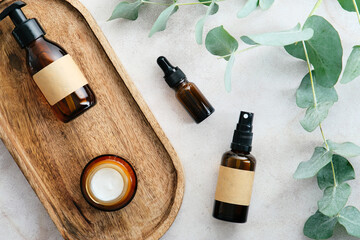 Skin care cosmetics set with eucalyptus branches on stone table in bathroom top view. Amber glass...