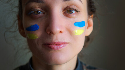 Indoor portrait of young girl with blue and yellow ukrainian flag on her cheek wearing military uniform, mandatory conscription in Ukraine, equality concepts
