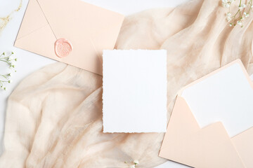Wedding invitation card mock-up. Flat lay blank paper card, envelopes, flowers on beige fabric....