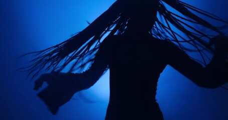 Silhouette of young woman dancing in blue light and smoke - Powered by Adobe