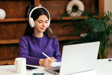 Young woman in purple sweater and headphones with laptop doing homework. education and business concept. remote work and freelance work. home interior