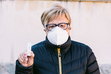 Elderly lady on the street, wearing a white mask, with a negative antigen test. Concept covid-19,...