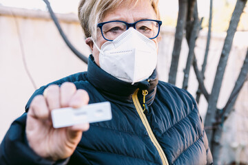 Elderly lady on the street, wearing a white mask, with a negative antigen test. Concept covid-19,...